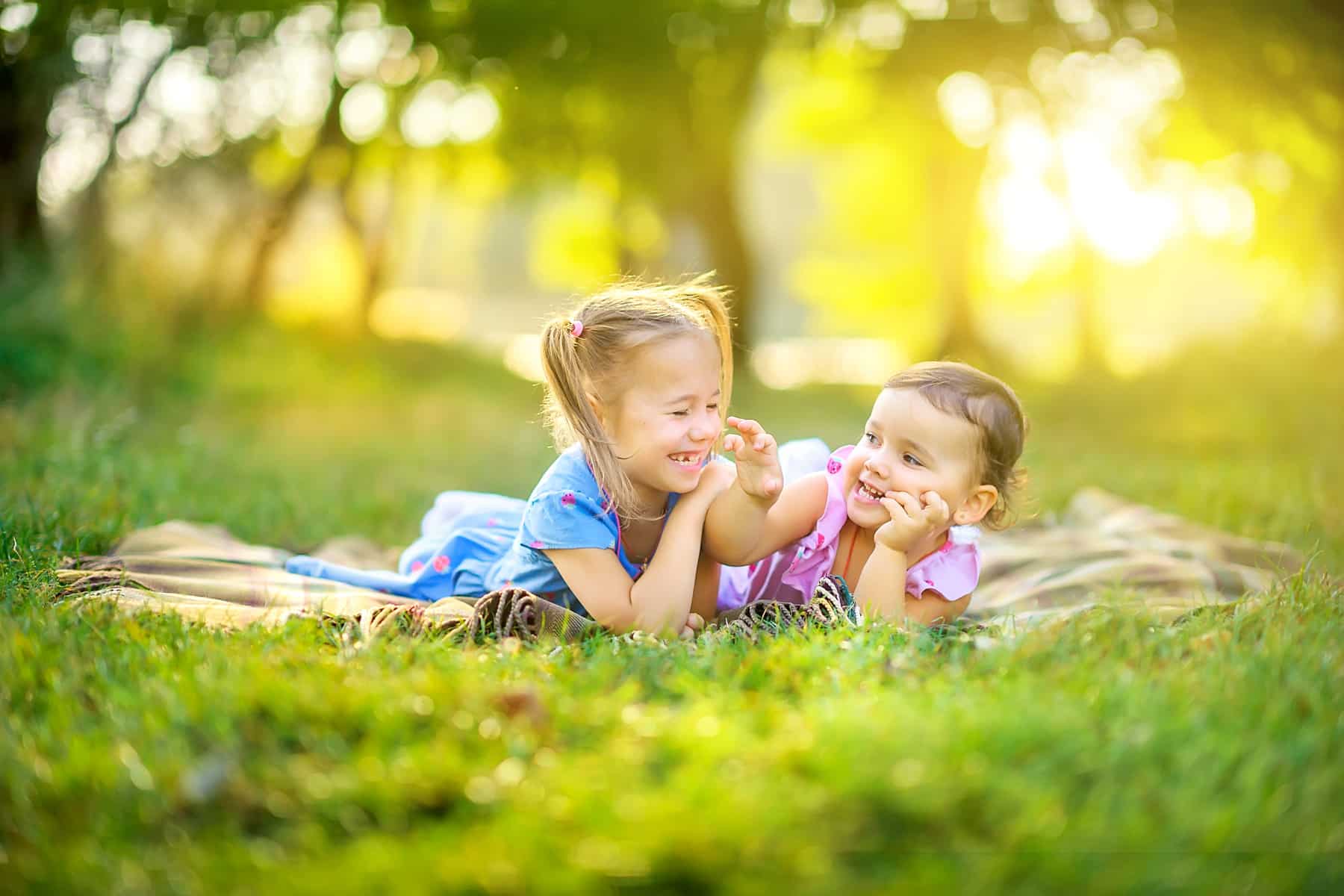 Cute children play in the park at sunset. Girls are lying on the grass playing and having fun. Children play and have fun outdoors. learn about special needs pediatric dentistry with tips from Honey Bee pediatric Dental Co in Lawrence, Lenexa, and Prairie Village
